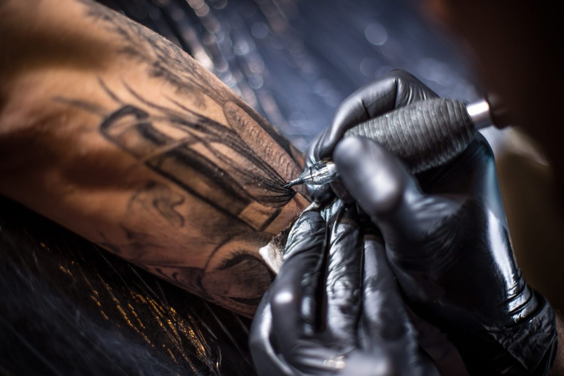 A professional tattoo artist introduces black ink into the skin using a needle from a tattoo machine.